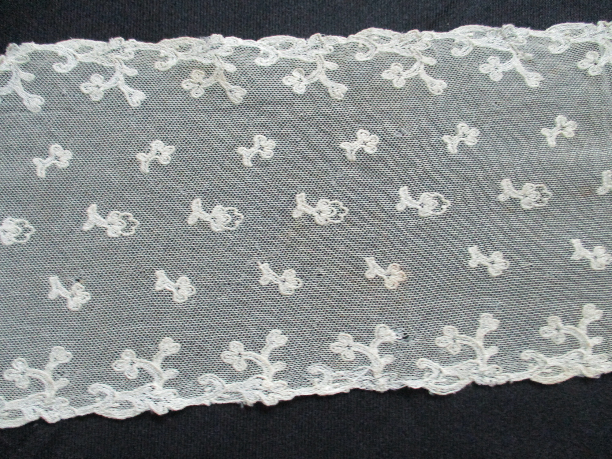 Cream lace sash.: Embroidered detail on cream lace sash.
