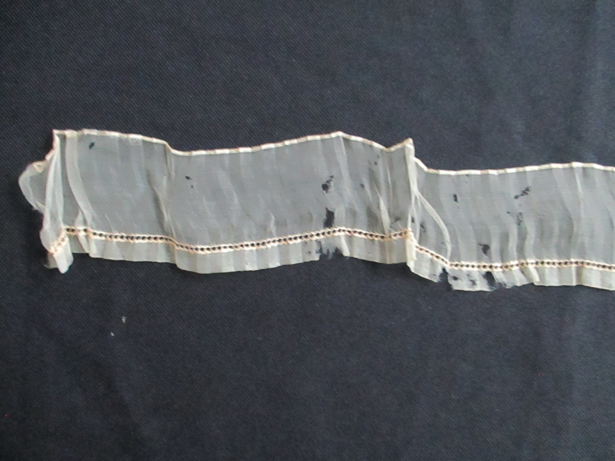 Piece of cream silk edging/trim.: End detail of cream silk ribbon/ edging on black background.