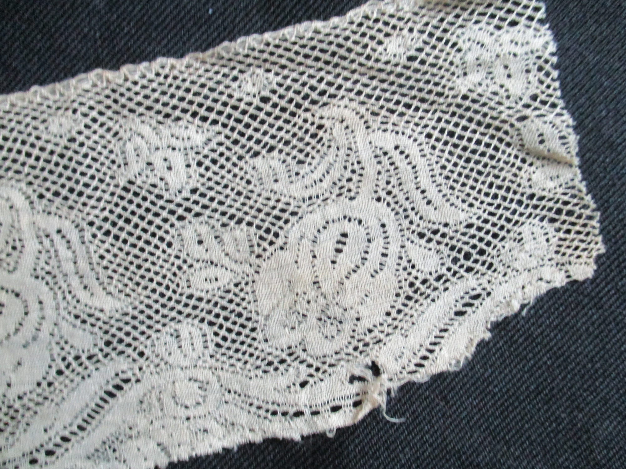 Piece of cream silk lace edging.: End detail of lace edging.