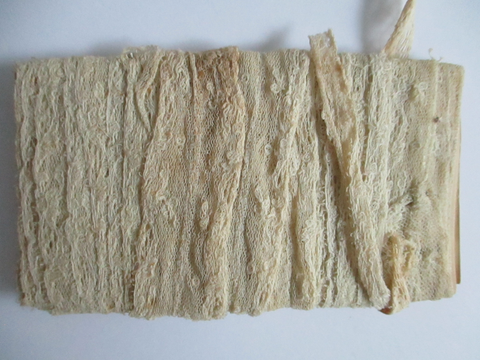 Unused length of lace trim/ribbon wound round paper.: Length of unused cream lace ribbon wound round paper.(ii)