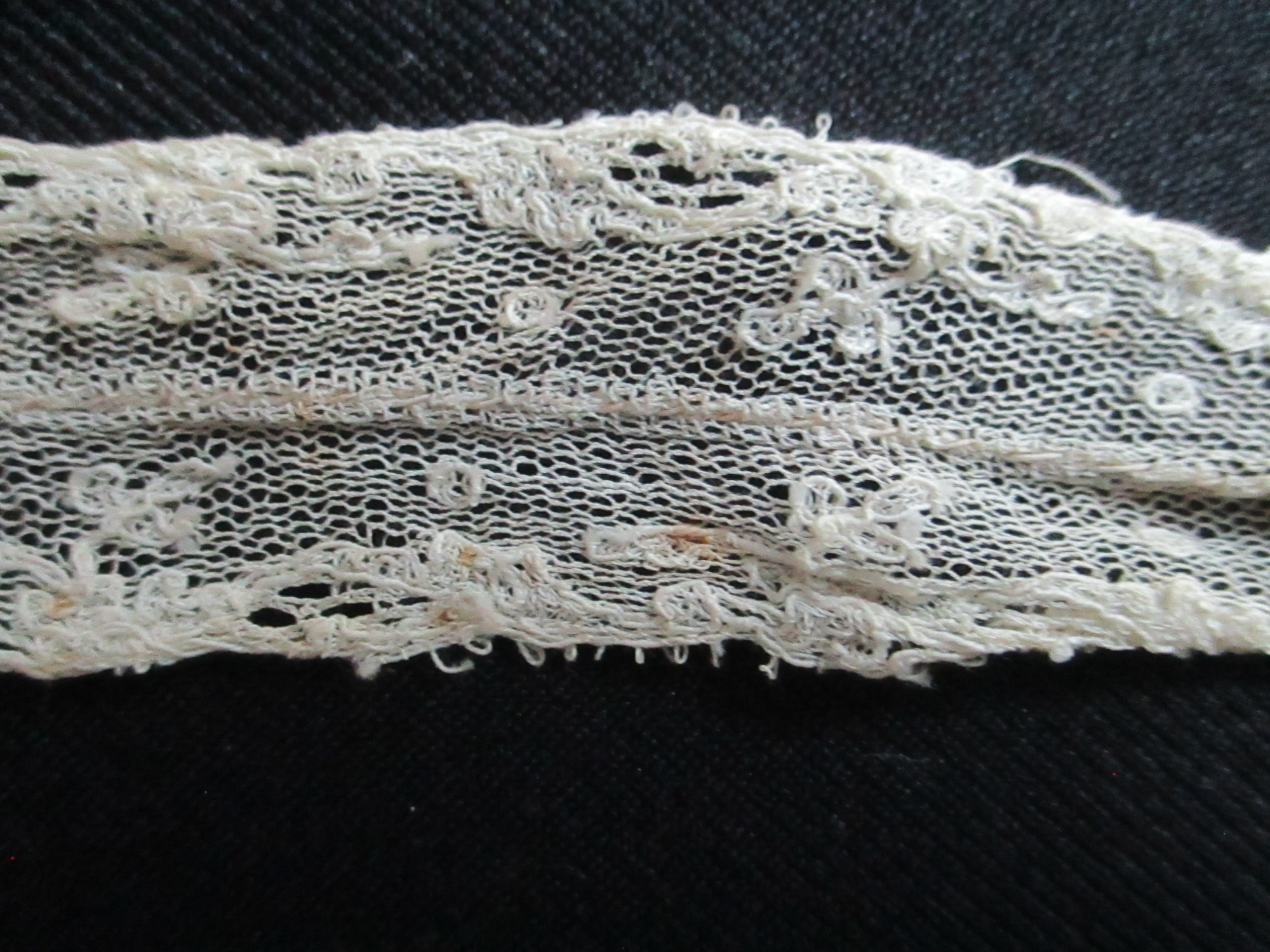 Unused length of lace trim/ribbon wound round paper.: Embroidery detail of cream lace ribbon.